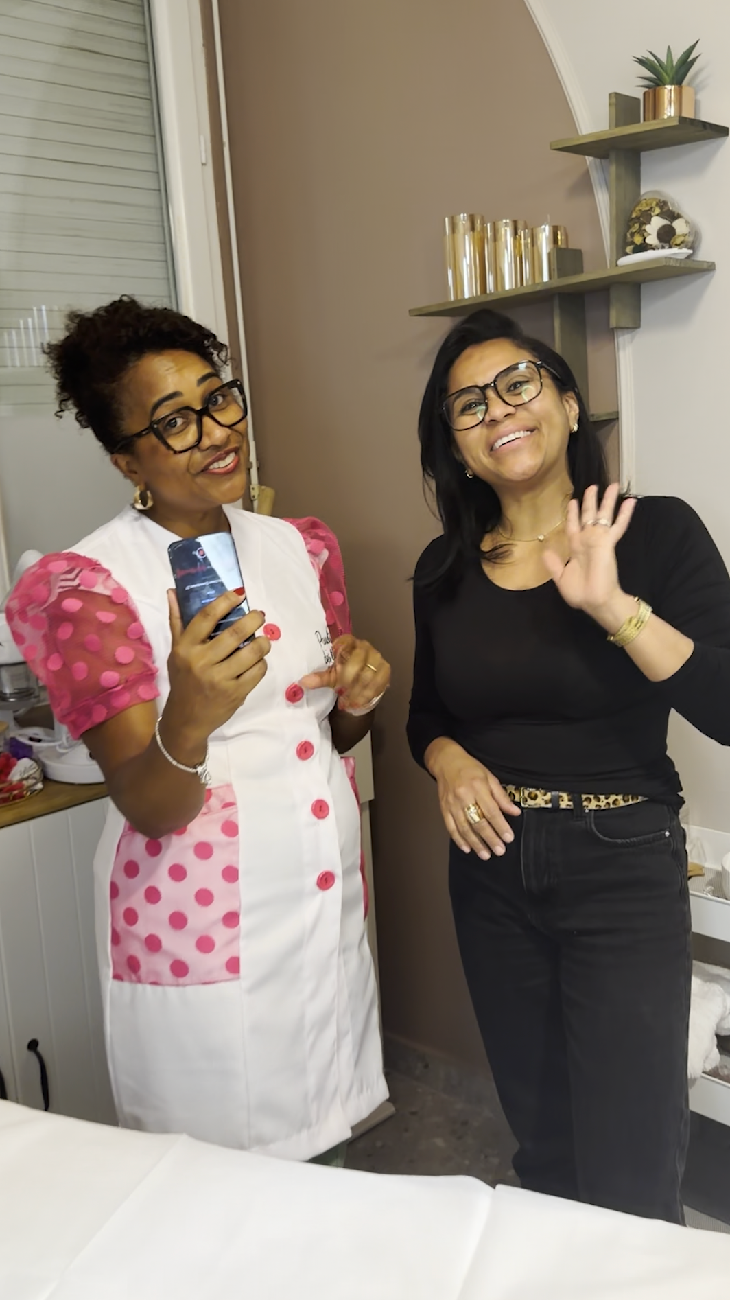 Deux femmes souriantes dans une cabine de soin Emioli, l’une saluant de la main