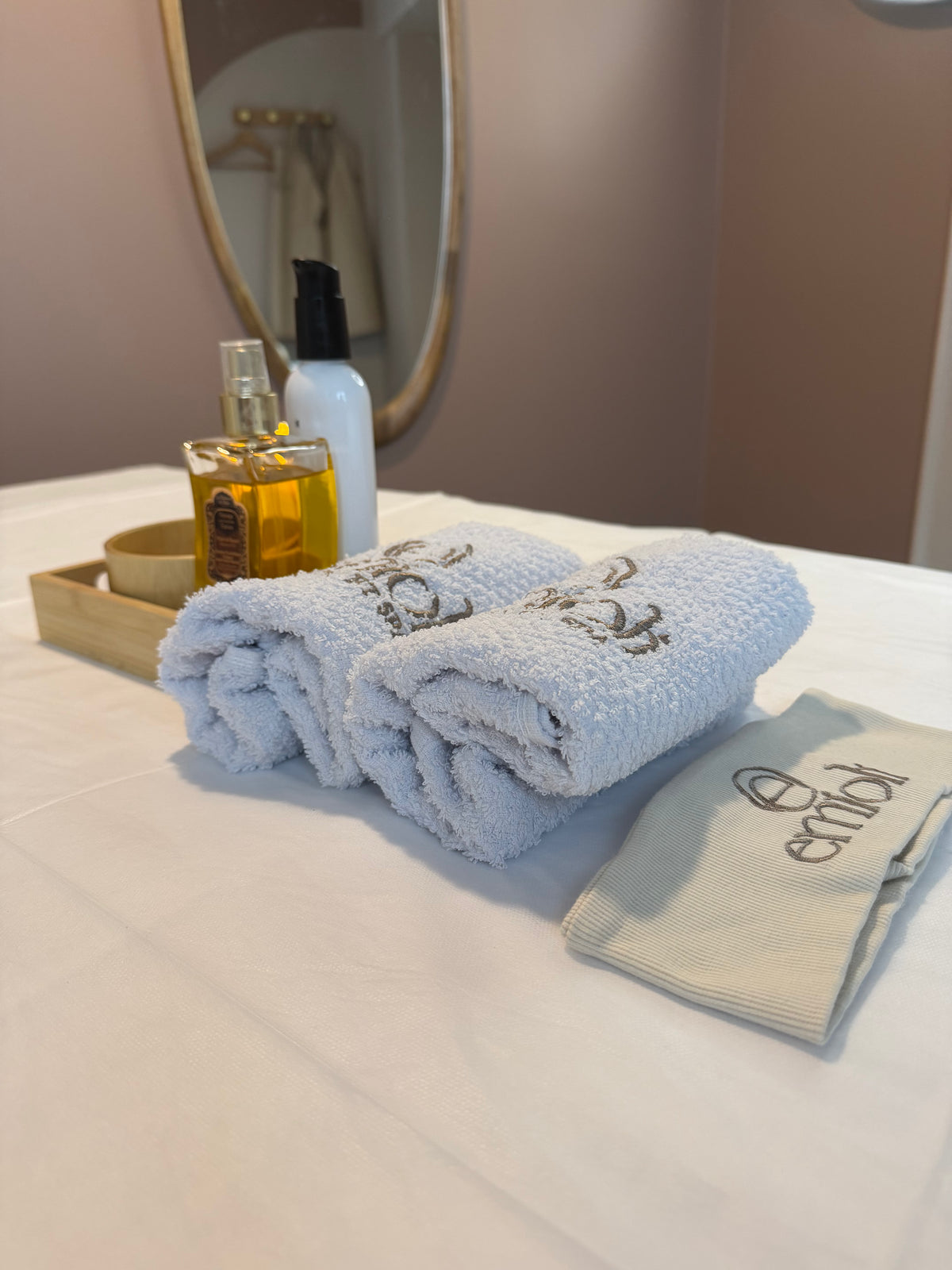Serviettes éponge brodées Emioli, huile de massage et bandeau posés sur une table de soin